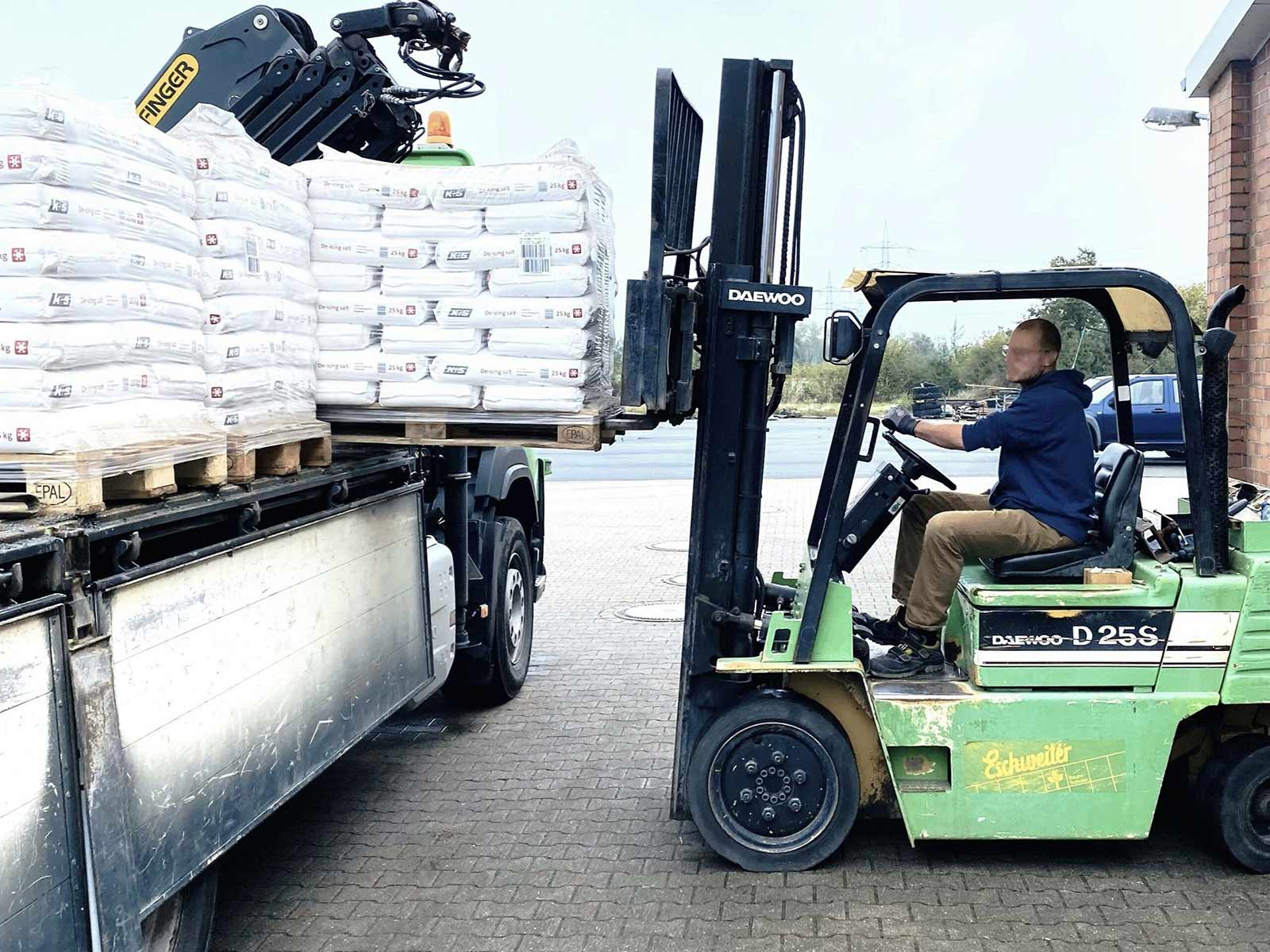 Arbeiter auf einem Gabelstapler verlädt Paletten mit Streusalzsäcken von einem Lkw zur Winterdienstvorbereitung