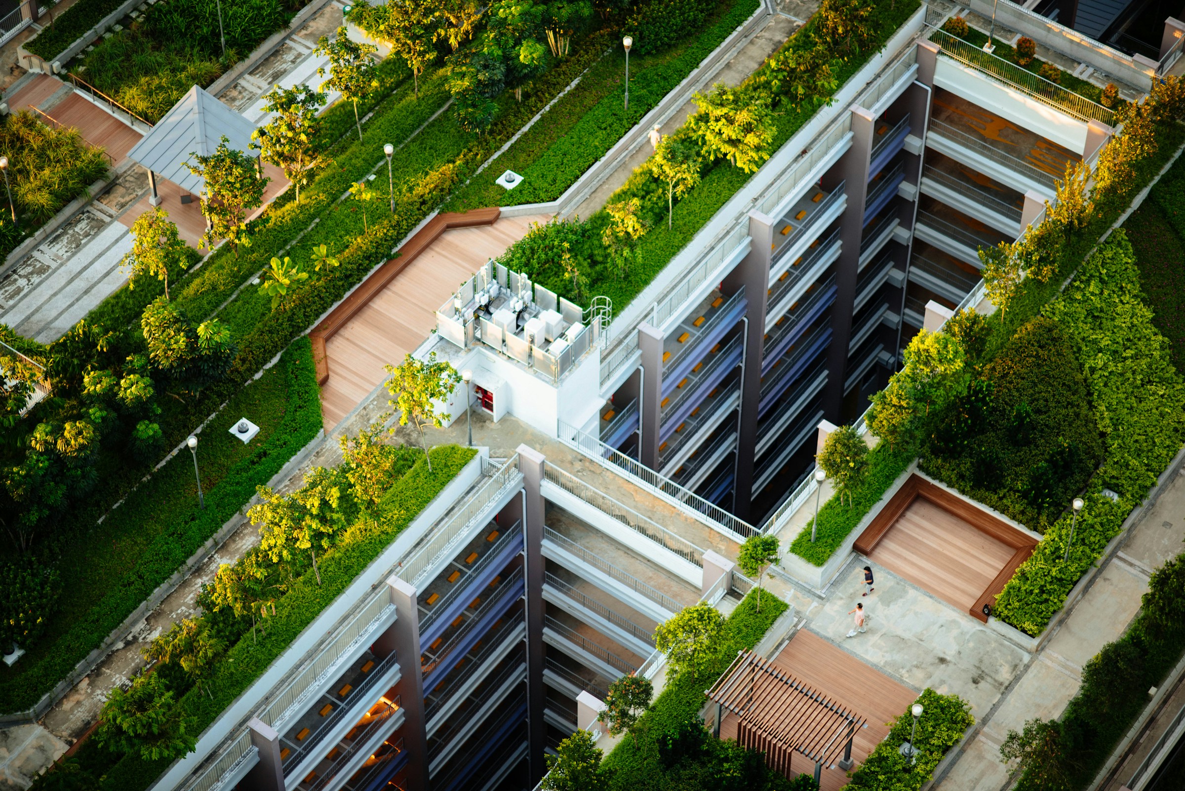 Vogelperspektive auf ein modernes Gebäude mit begrünten Dachterrassen und Gehwegen zwischen üppiger Vegetation.